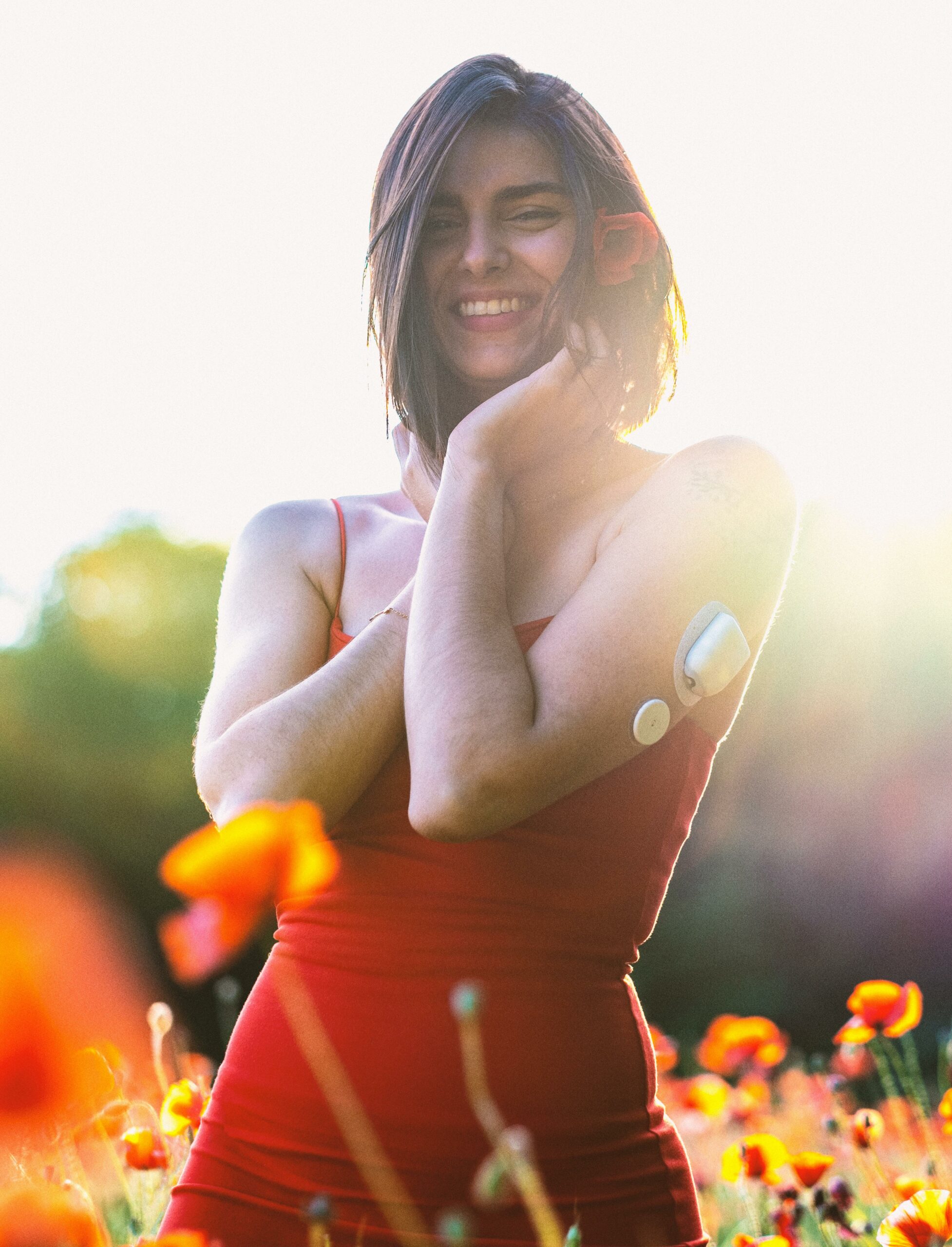 Femme souriante dans un champ de fleurs avec un capteur de glycémie, symbole d’équilibre et bien-être pour le diabète.