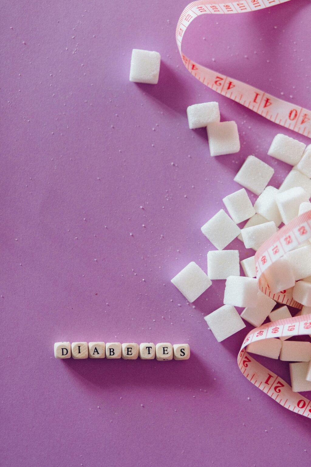 Gros plan sur sucre en vrac, ruban métrique et mots “diabetes” en dés, symbolisant la gestion du sucre et du diabète.