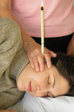 Séance de bougie d’oreilles : femme allongée recevant un soin de bien-être avec une bougie auriculaire allumée
